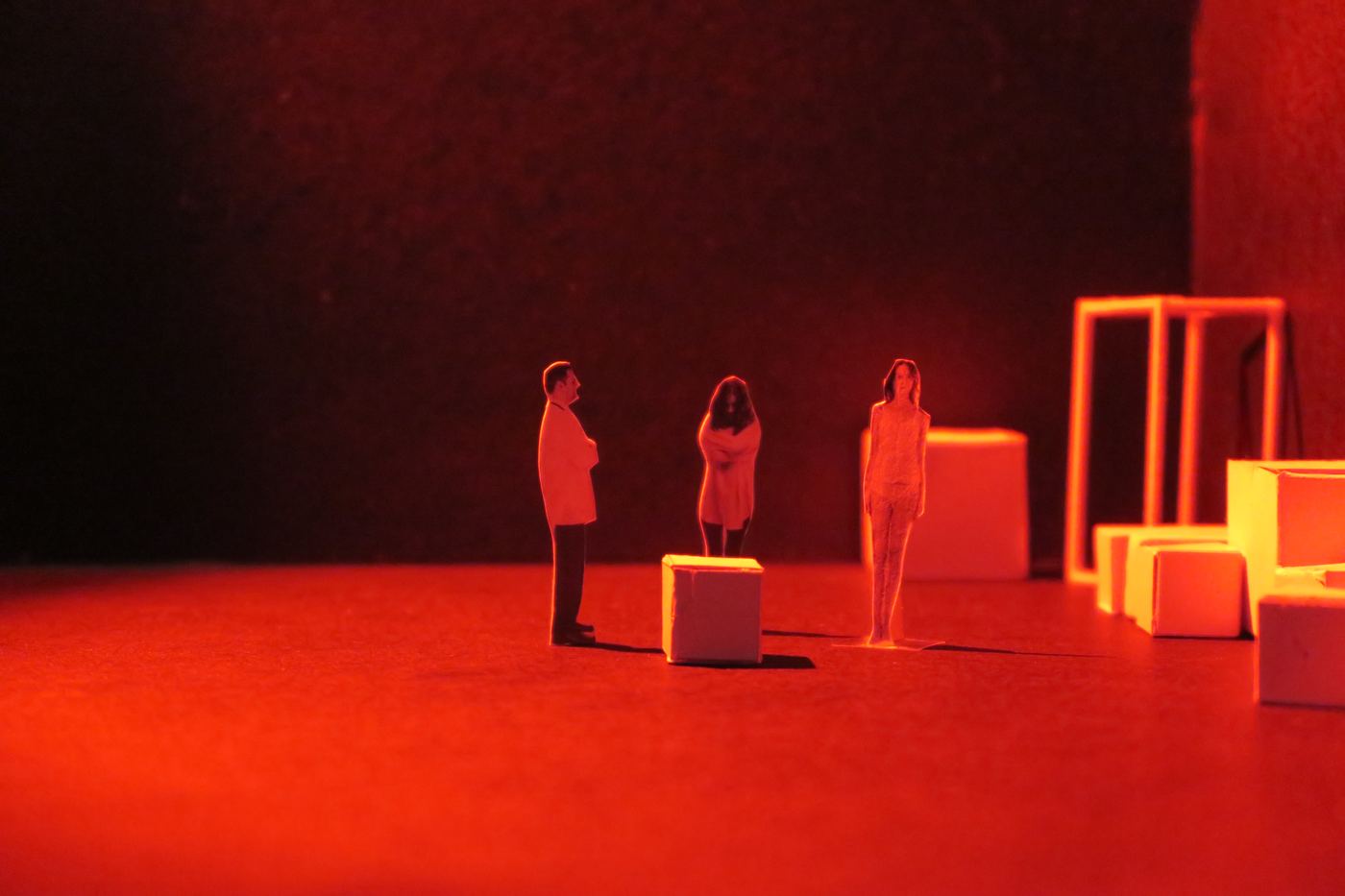 Scale model: white paper cubes and wooden frames with small cut-out figures under purple light